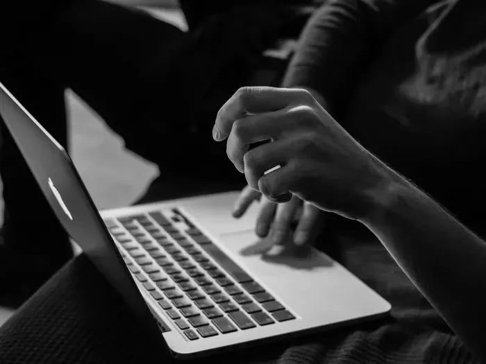 Close-up black and white photo of hands typing on a laptop keyboard while working on a project indoors on Town Service Spot